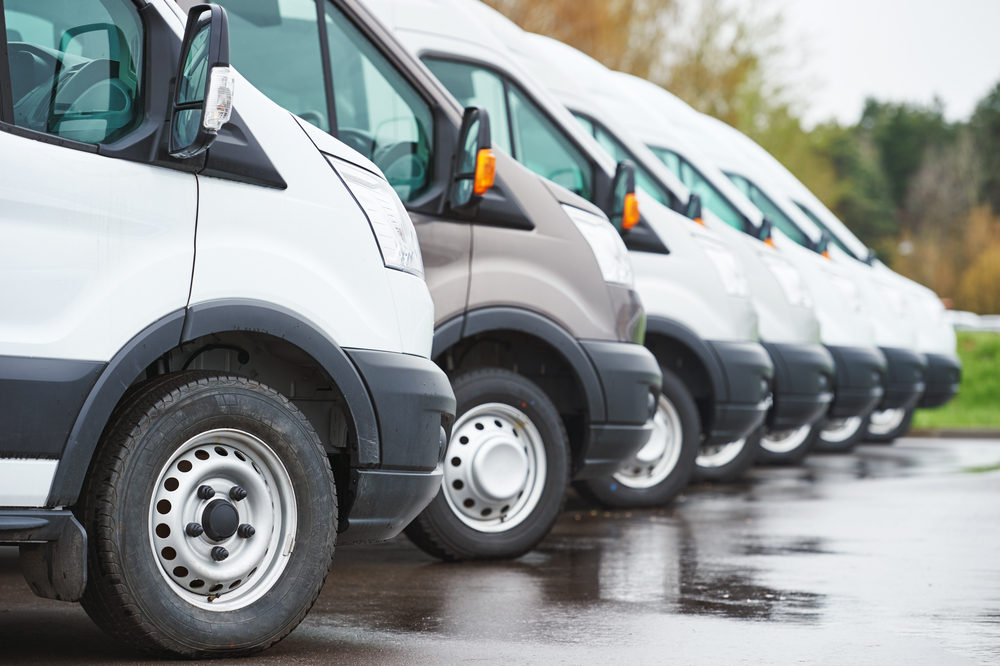 A row of commercial cargo vans parked diagonally in a line on wet asphalt