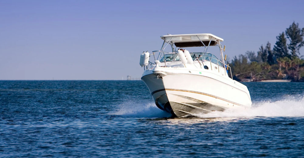 A white motorboat speeds across blue water, creating a wave. - https://johnpierceinsurance.com/
