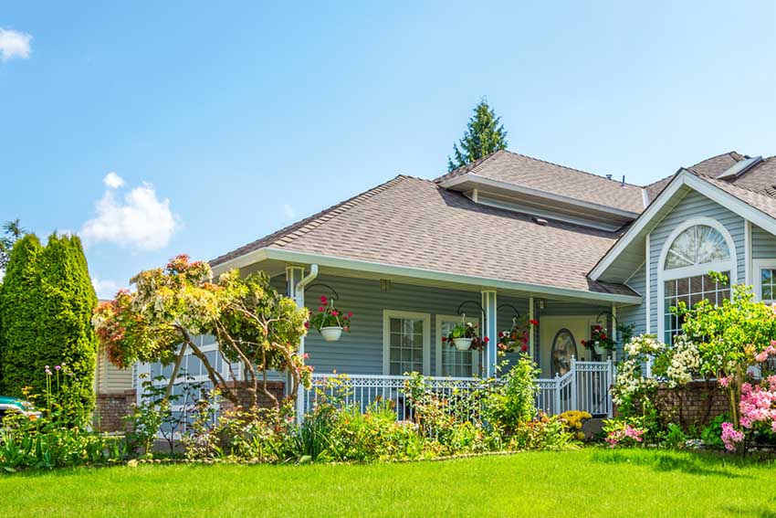 Front view of a light blue suburban house with a well-maintained garden - https://johnpierceinsurance.com