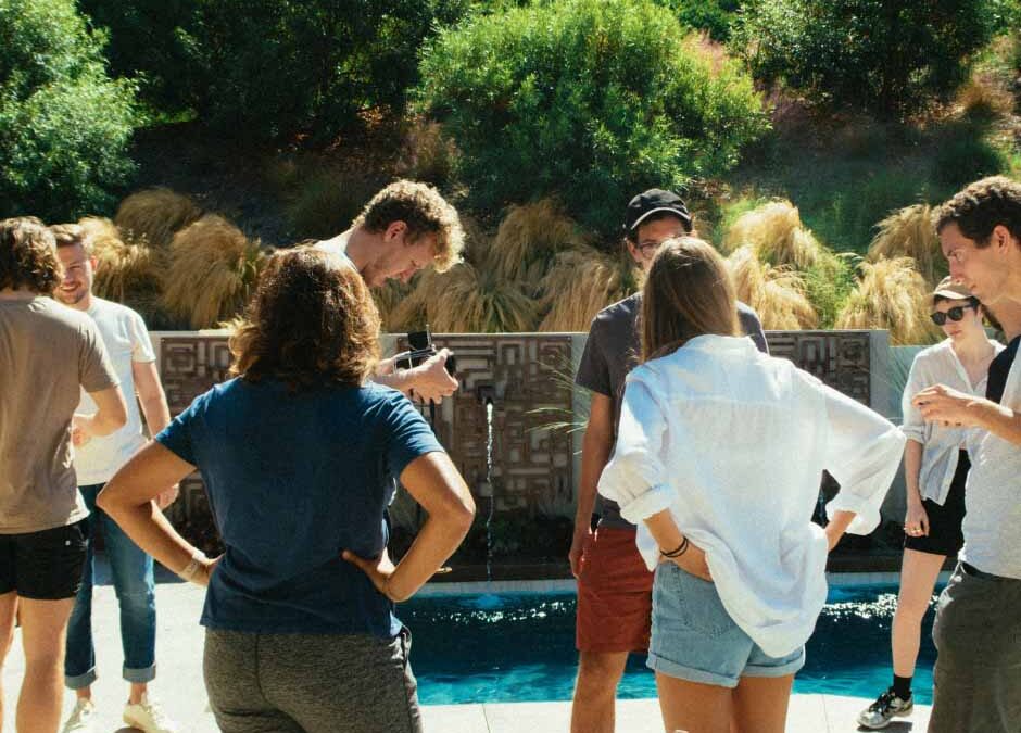 A group of five people standing together around a swimming pool, enjoying a sunny day outdoors