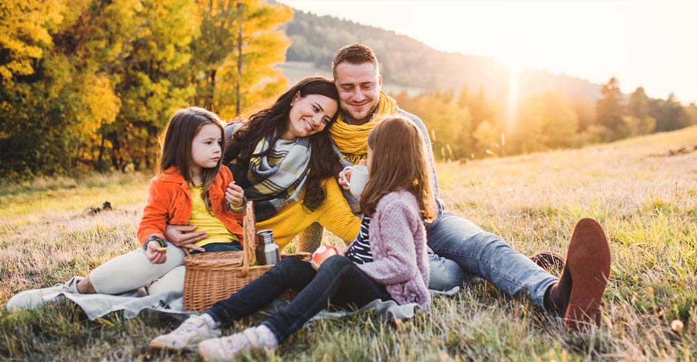 A family enjoying a picnic together in a sunlit autumn meadow.